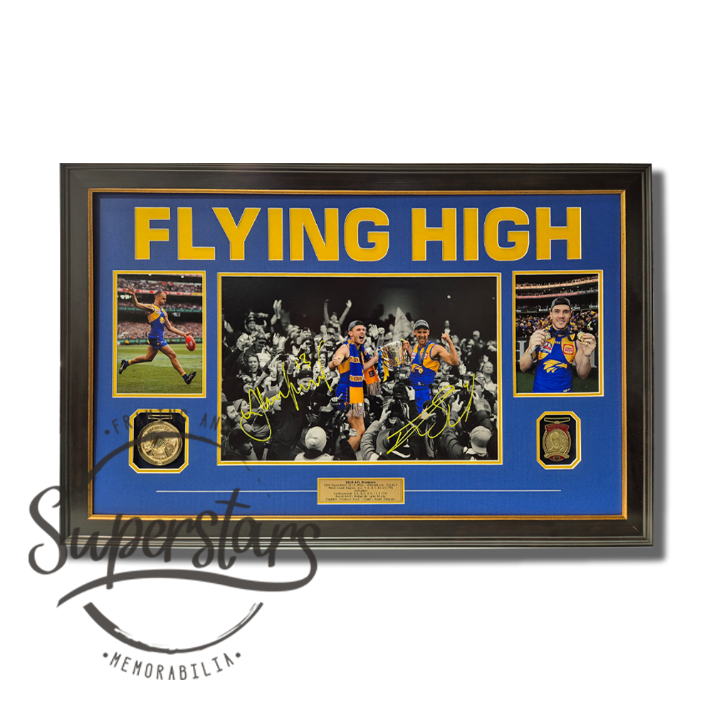 Dom Sheed and Luke Schuey Memorabilia. The words Flying High are cut into the blue matboard to reveal yellow letters across the top. In the centre is a photo of the the media and fans with Dom Sheed and Luke Shuey being carried and in full colour, the rest are black and white. Dom and Luke have signed the photo using yellow ink. To the left there is a smaller photo of Dom Sheed kicking the football during a game, it has a yellow border. Below it is a replica AFL premiership medal. To the left is a portrait photo of Luke Shuey wearing his Premiership Medal and Norm Smith medal. Below that is a replica Norm Smith medal. At the bottom of the frame is a gold plaque which is engraved with the highlights of the 2018 Grand Final. A yellow line is etched into the blue border on both sides of the plaque. The frame is black timber with a rustic gold trim.